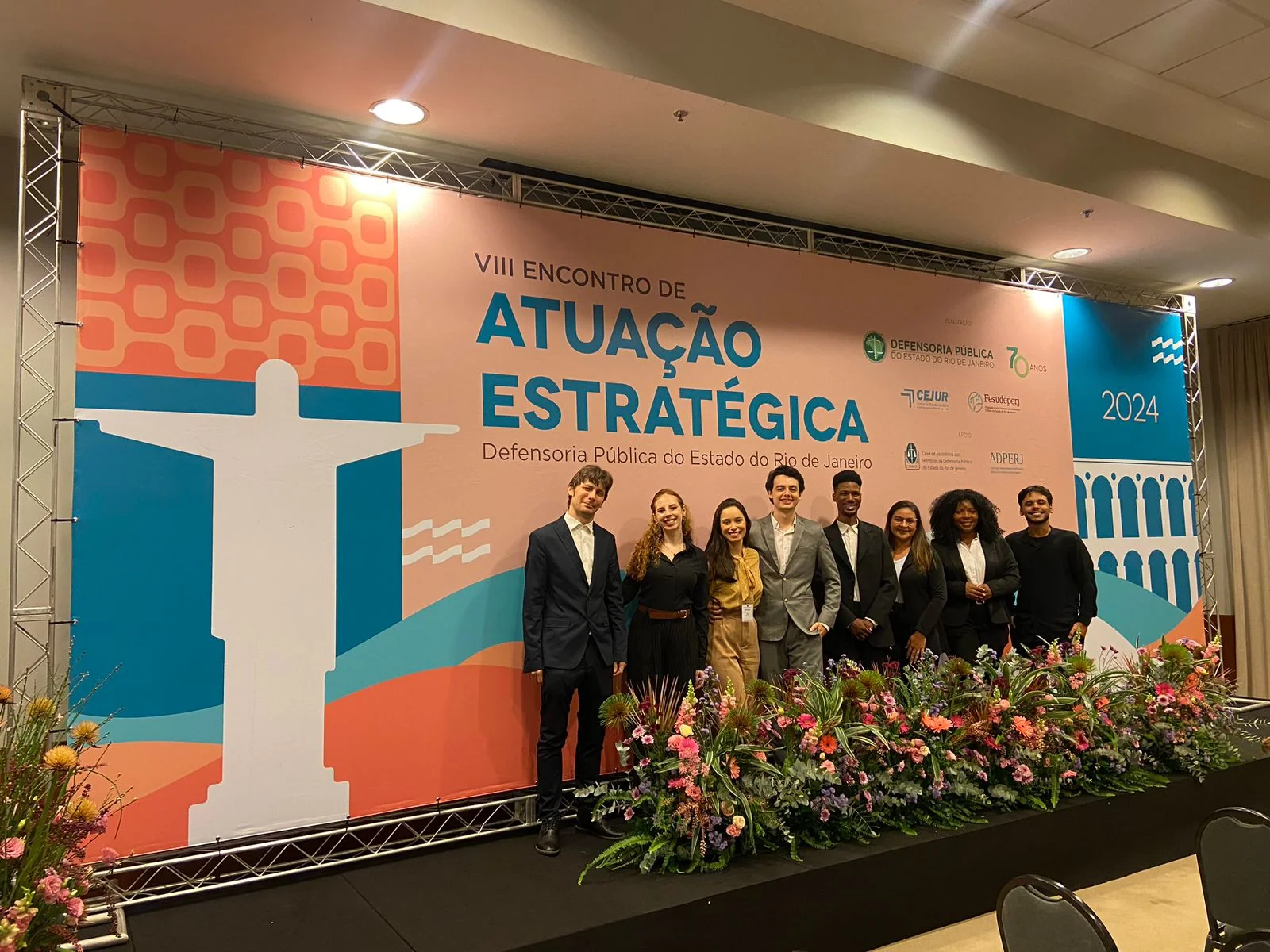 Equipe de recepção posa diante do painel do VIII Encontro de Atuação Estratégica.