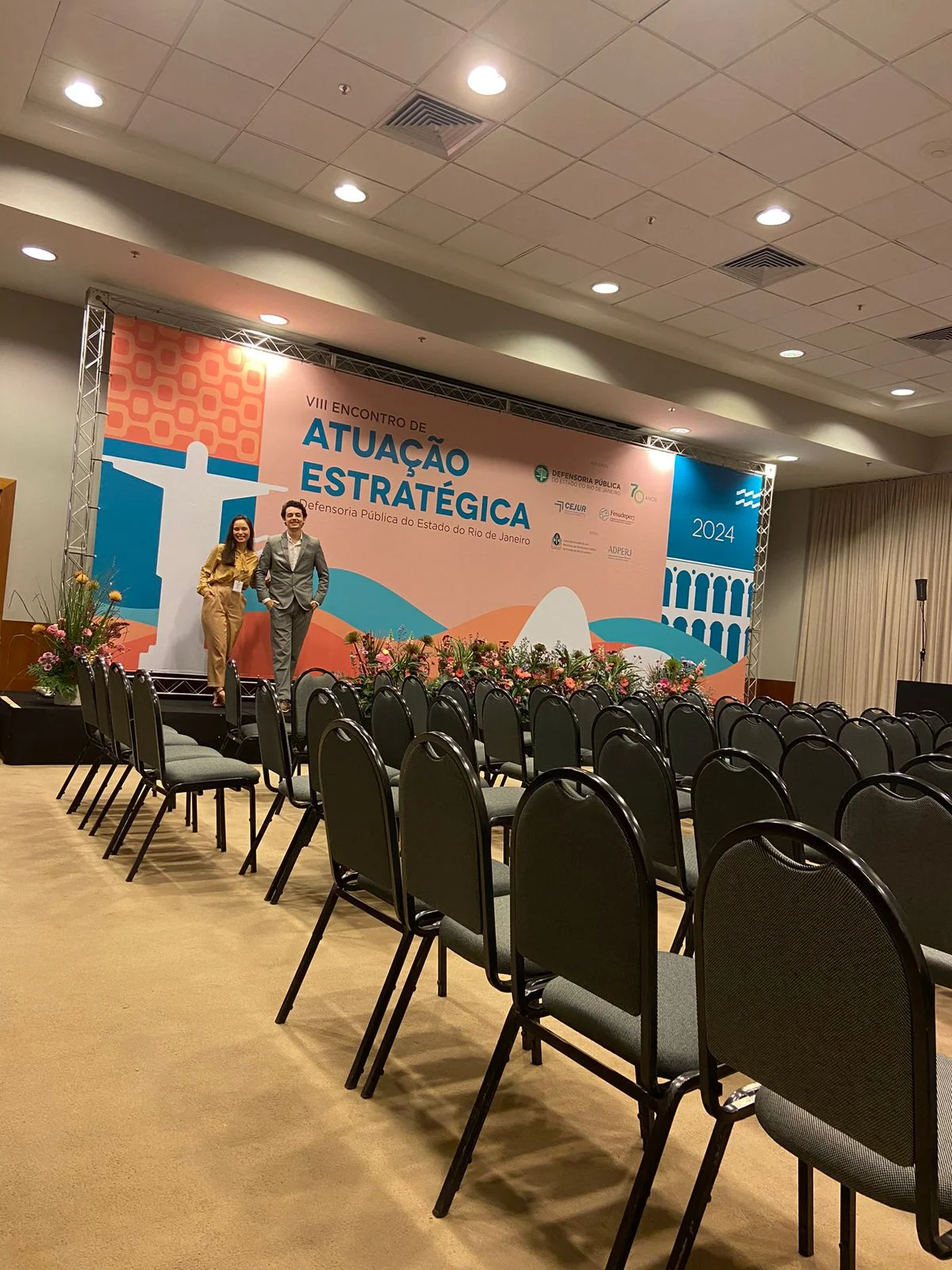 Salão com fileiras de cadeiras voltadas para o palco e o painel do encontro.
