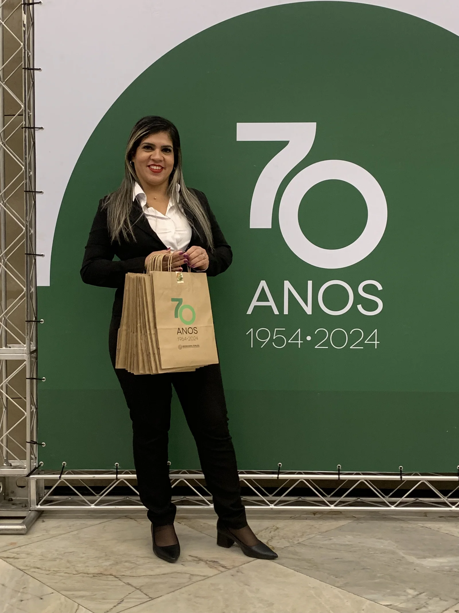 Recepcionista com kit comemorativo diante do painel dos 70 anos.