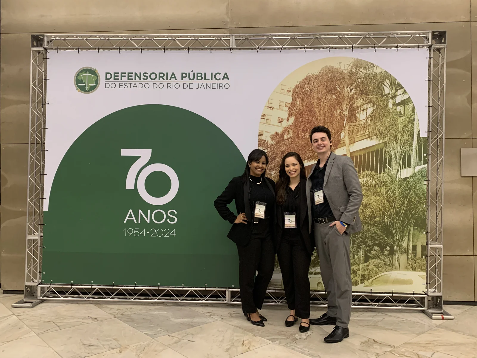 Equipe de recepção diante do painel comemorativo dos 70 anos da Defensoria.