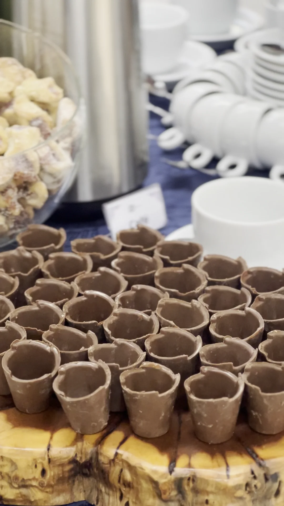Copinhos de chocolate, taça com petit fours, xícaras organizadas e garrafa térmica na mesa de café.