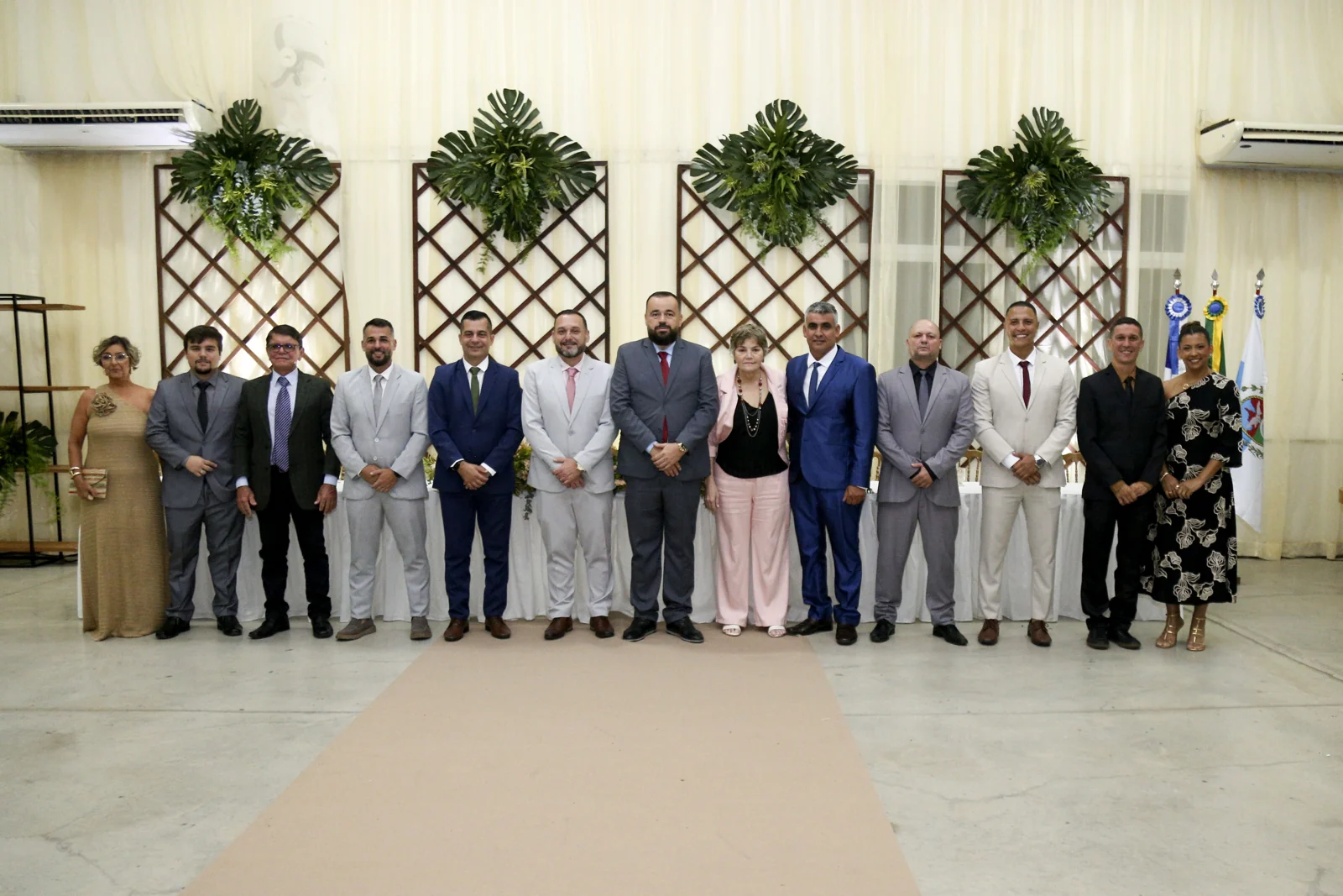 Participantes posando em grupo diante da mesa e da decoração da sessão solene de Itaocara
